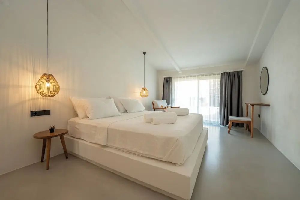 Helles Schlafzimmer mit einem großen Doppelbett, Holzmöbeln und Fenstervorhängen.
