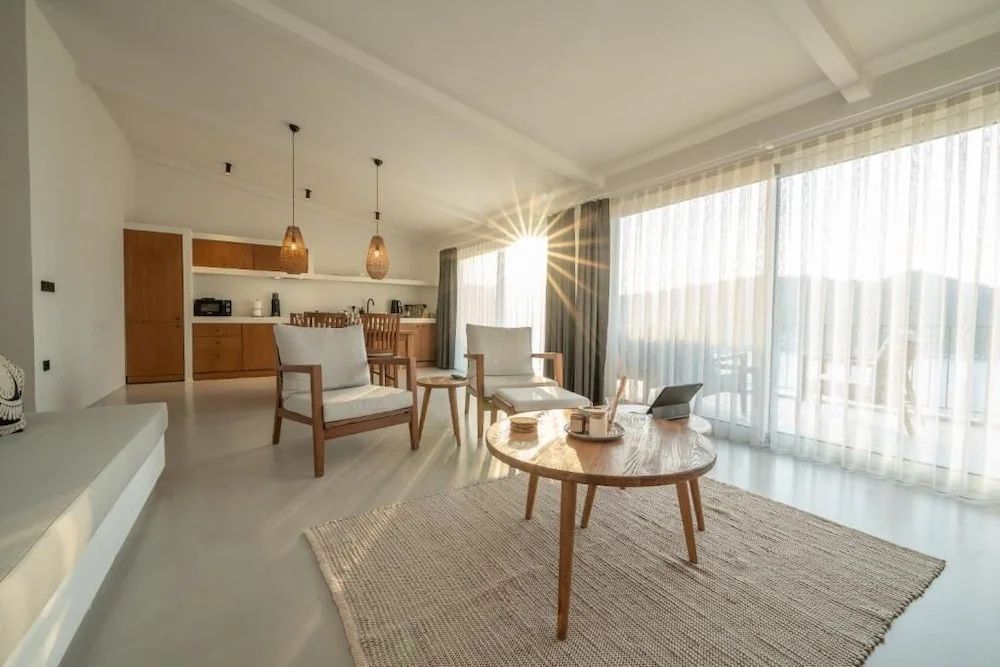 Sonnendurchfluteter Wohnbereich mit Sesseln Holztisch und großer Fensterfront.
