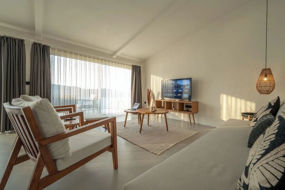 Helles Wohnzimmer mit Fernseher, Couchtisch und Zugang zum Balkon.