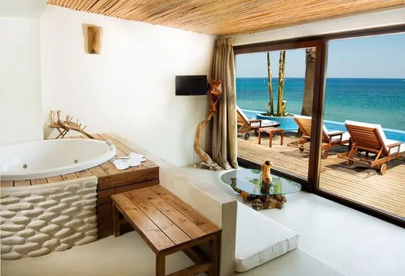 Suitenbereich mit Whirlpool, Holzdecke und große Glasfront mit Blick auf Meer und Terrasse.