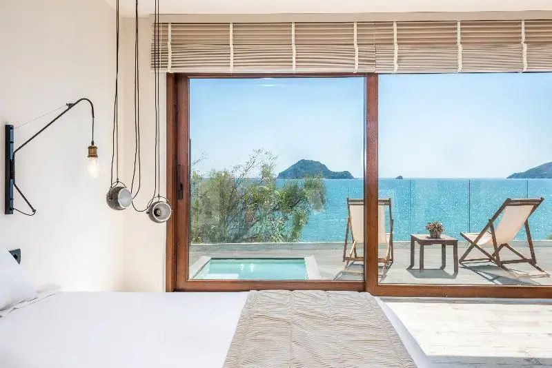 Blick durch eine große Glasfront auf das Meer, eine kleine Insel und die Terrasse mit Tauchbecken.