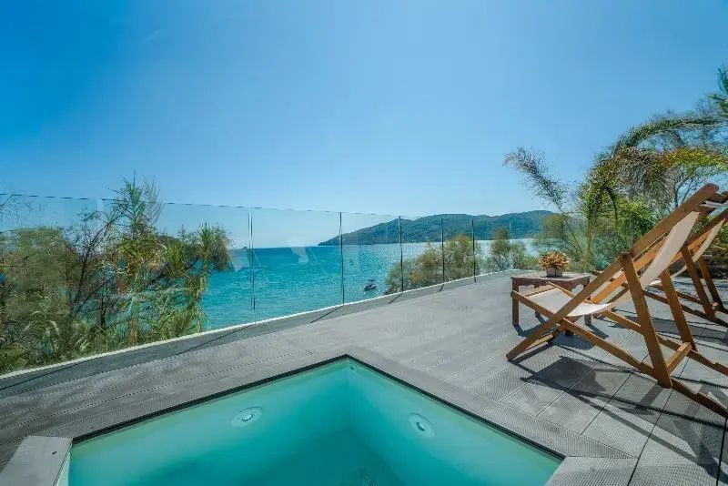 Terrasse mit Glasgeländer, kleinem Pool im Boden, Holzliege und Blick auf das blaue Meer.