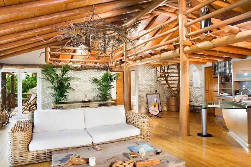 Loungebereich mit rustikaler Holzdecke, hellem Sofa, Holzfußboden und Pflanzen.