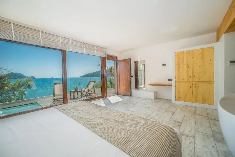 Helles Hotelzimmer mit großem Bett und Blick durch Panoramatüren auf das Meer.