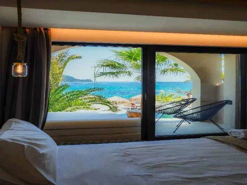 Blick aus dem Hotelzimmer über die Terrasse hinweg auf das blaue Meer und Palmen.