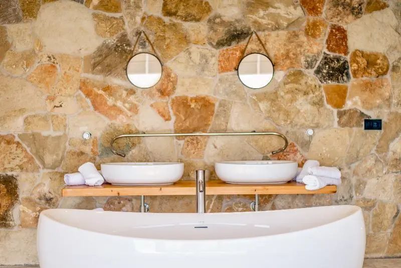 Doppelwaschtisch mit zwei runden Spiegeln vor einer Natursteinwand im Badezimmer.