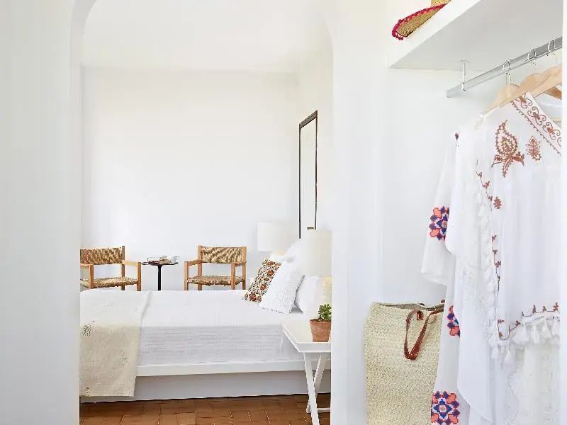 Weiß eingerichtetes Schlafzimmer mit großem Bett und Sitzgelegenheit.