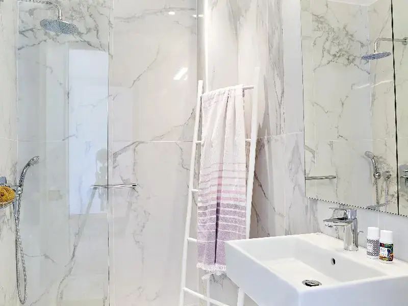 Helles Badezimmer in Marmoroptik mit Waschbecken, Dusche und Handtuchhalter.