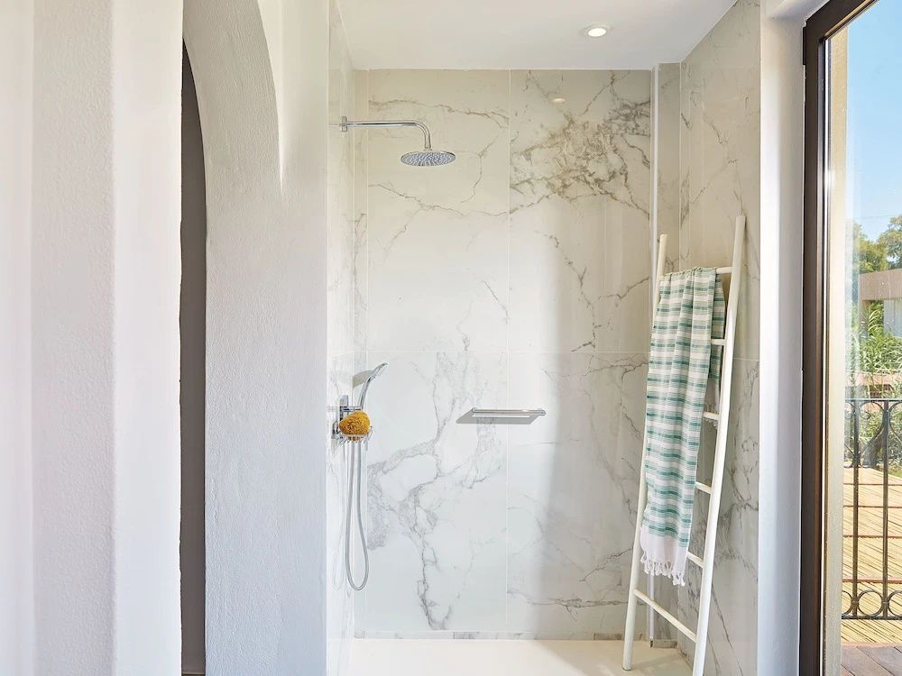 Badezimmer mit begehbarer Dusche, Marmorwänden und dekorativer Holzleiter.