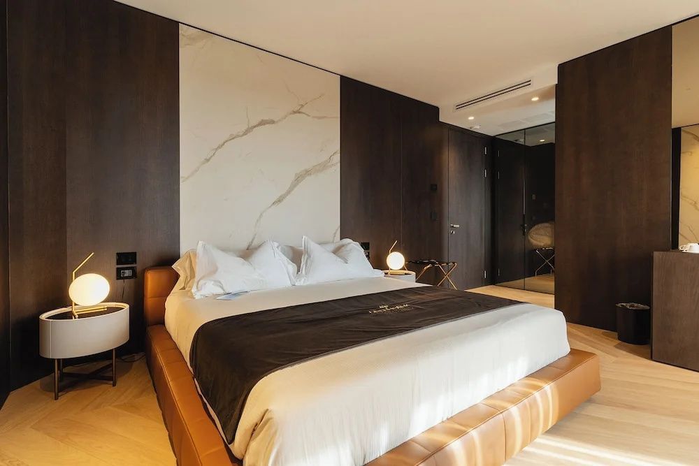 Doppelbett mit braunem Lederrahmen, weiße Kissen und marmoriertes Wandpaneel im Schlafzimmer