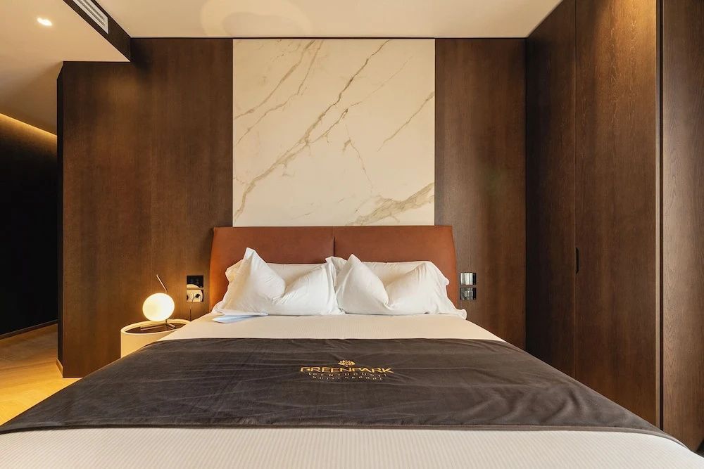 Doppelbett mit braunem Kopfteil, weißen Kissen und Marmorelement an der Holzwand.