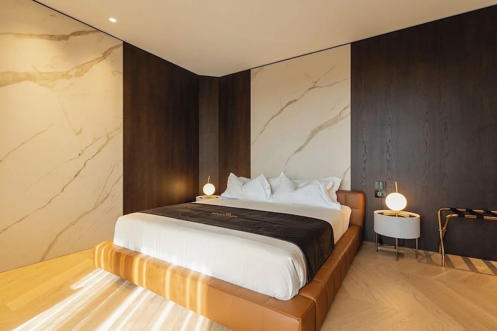 Hell erleuchtetes Schlafzimmer mit modernem Doppelbett, Nachttischen und Marmorwand