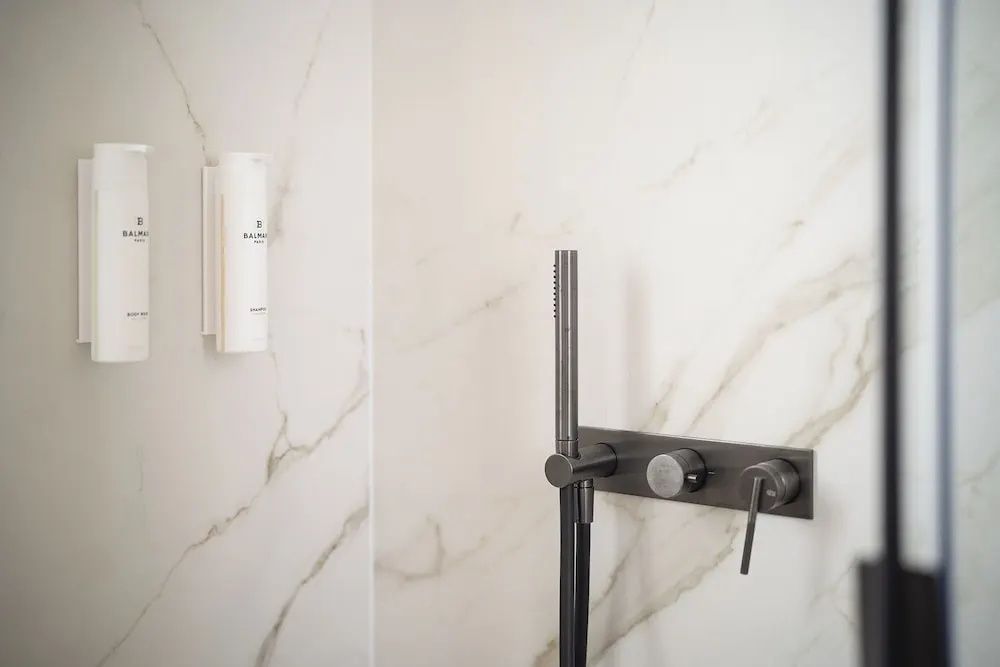 Schwarze Duscharmatur und Handbrause an einer hellen Wand in Marmoroptik.