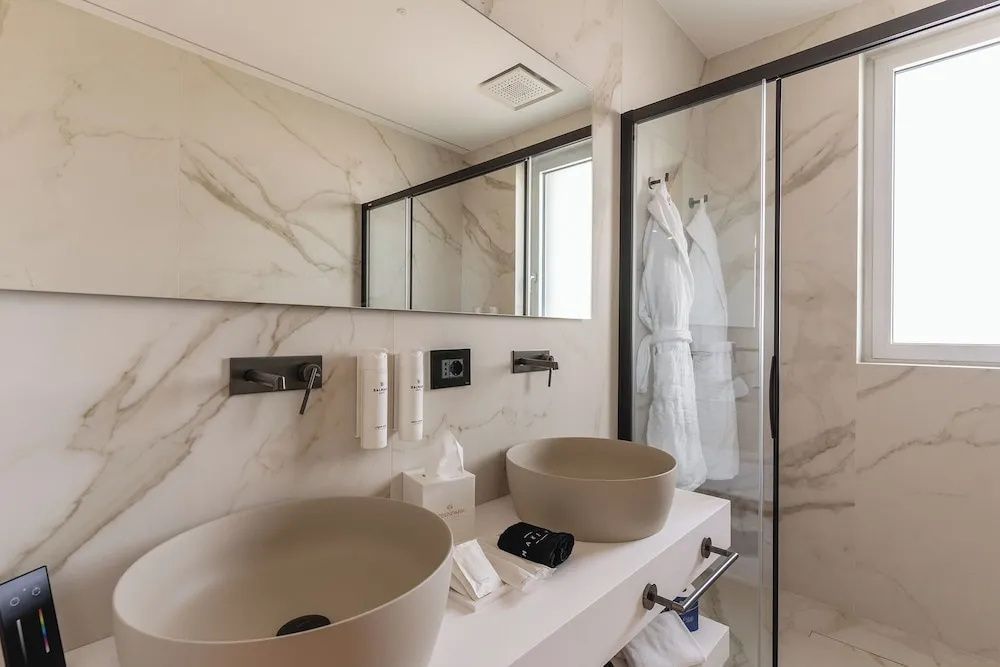 Badezimmer mit zwei Aufsatzwaschbecken, großem Spiegel, Dusche und aufgehängten Bademänteln.
