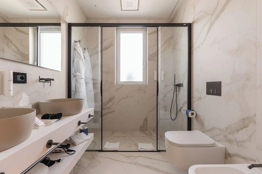 Modernes Badezimmer mit transparenter Duschkabine, hellem Marmor und weißem WC.