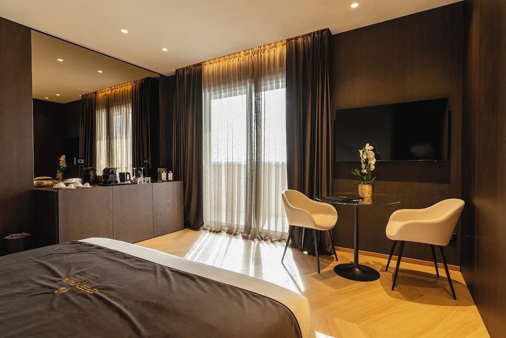 Sitzbereich im Zimmer mit zwei hellen Stühlen, Glastisch und Wandfernseher.