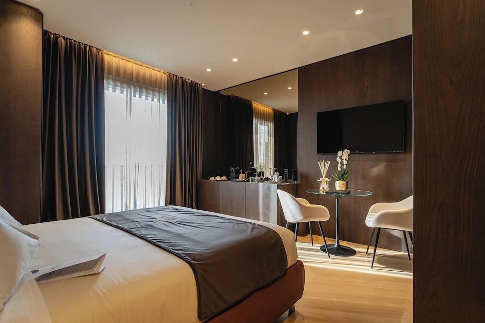 Schlafbereich der Suite mit Doppelbett, Flachbildfernseher, Sitzgelegenheit und Holzfußboden.