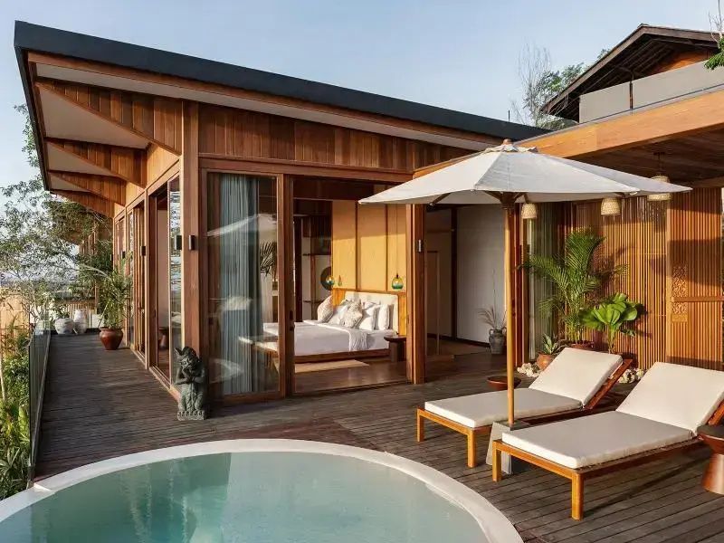 Holzterrasse einer Villa mit zwei Sonnenliegen, Sonnenschirm und rundem Pool.