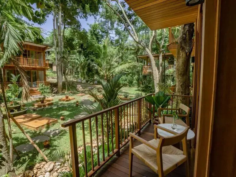 Blick von einem Holzbalkon mit Sitzmöbeln auf die grüne Gartenanlage des Resorts.