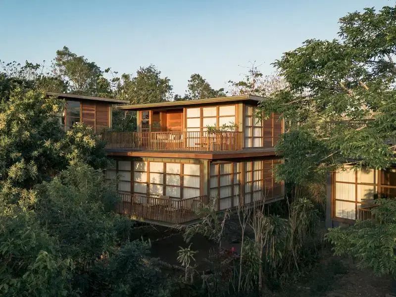 Zweigeschossige Holzvilla mit Balkon mitten in üppigen grünen Bäumen und Vegetation.