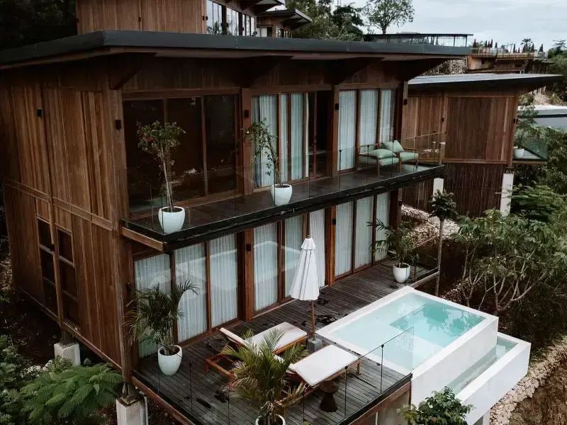 Zweigeschossiges Holzgebäude mit privatem Außenpool, Sonnenliegen und großem Balkon.