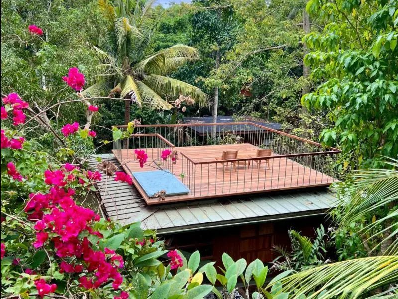 Holzdachterrasse mit Sitzgelegenheit inmitten von grünen Bäumen und rosa Blüten.