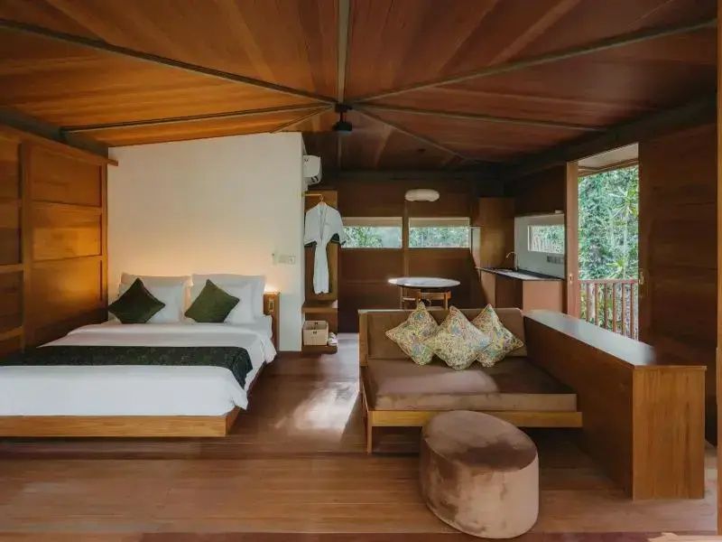 Schlaf- und Wohnbereich aus Holz mit einem Doppelbett, Sofa und hoher Holzdecke.