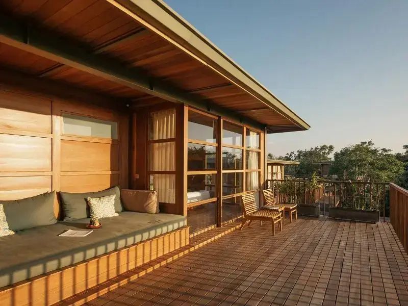 Holzterrasse einer Villa mit gepolsterter Sitzbank, Stühlen und großen Glasfronten.