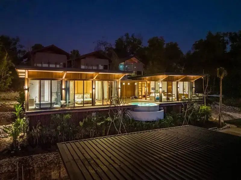 Beleuchtete Holzvilla des Resorts bei Nacht mit großen Glasfronten und Terrasse.