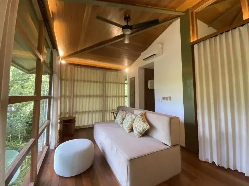 Wohnbereich mit hellem Sofa, Holzdecke, Deckenventilator und großen Fensterfronten.