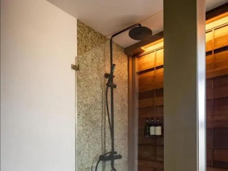 Moderne Dusche mit dunklem Regenduschkopf, Glaswand und Natursteinwand.