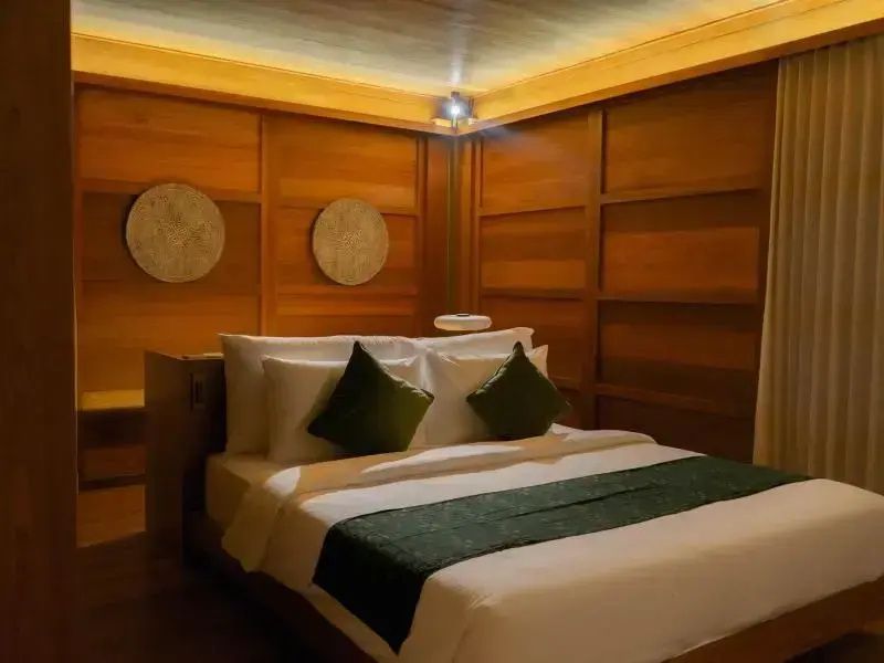Doppelbett mit grünen Kissen in einem holzverkleideten Schlafzimmer mit warmem Licht.