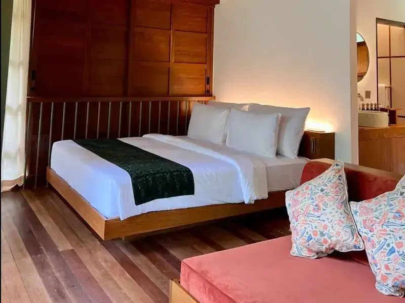 Doppelbett aus Holz mit weißer Bettwäsche und angrenzendem orangen Sofa aus Holz.