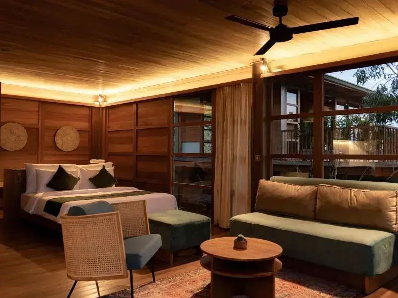 Wohnbereich einer Suite mit grünem Sofa, Sesseln, Holzmöbeln und Blick auf das Bett.
