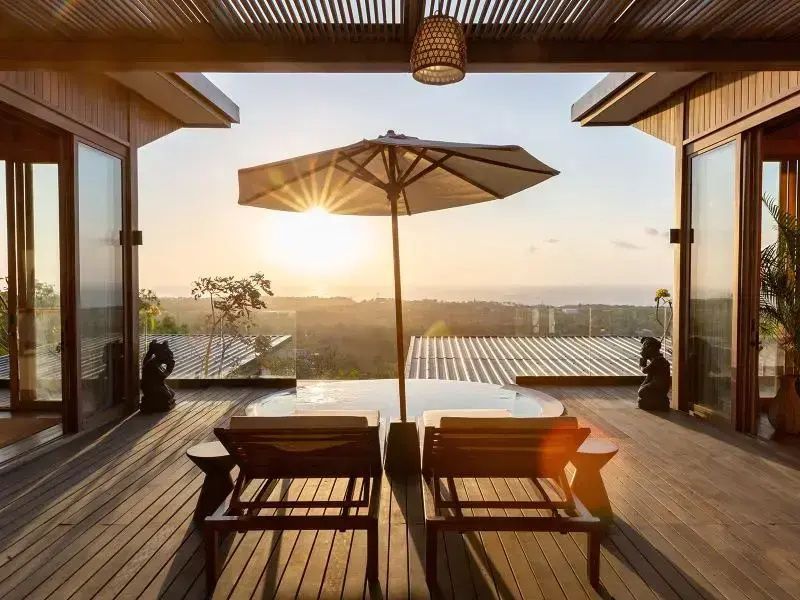 Blick von der Holzterrasse mit Liegestühlen auf den Sonnenuntergang über dem Meer.