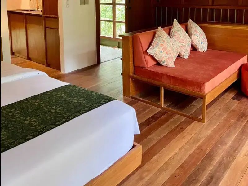 Sitzbereich mit orangem Holzsofa und gemusterten Kissen auf dunklem Holzboden.