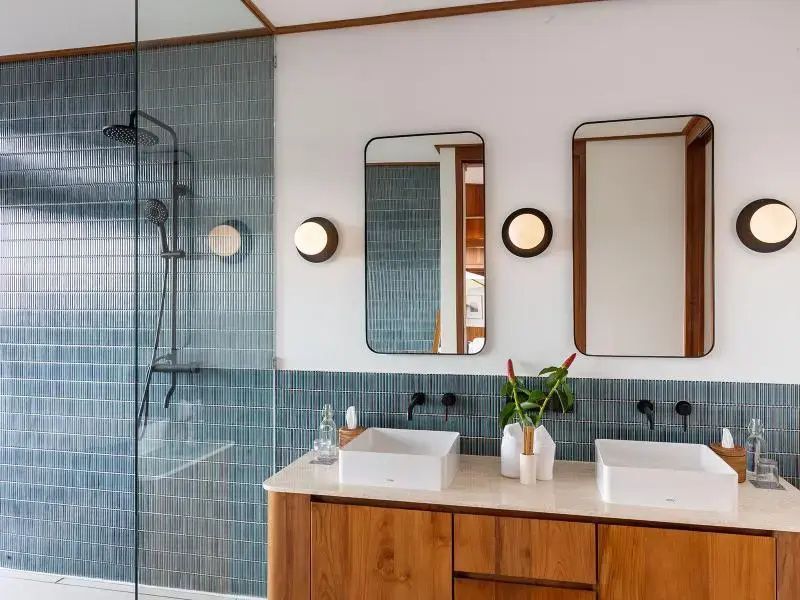 Modernes Badezimmer mit Holzwaschtisch, zwei Waschbecken, zwei Spiegeln und Regendusche.