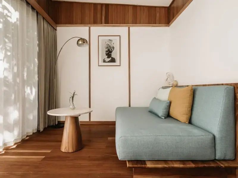 Wohnbereich mit mintgrünem Sofa, Holzverkleidung an der Wand und Stehlampe.