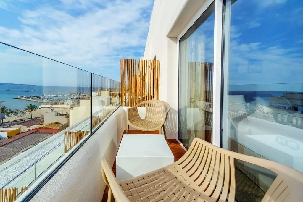 Balkon mit Glasgeländer, zwei Stühlen, kleinem Tisch und Weitblick auf Ort und Meer.