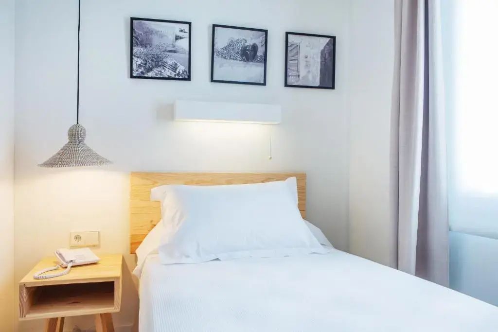 Weiß bezogenes Einzelbett mit hellem Holzkopfteil und drei Schwarzweißbildern an einer weißen Wand.