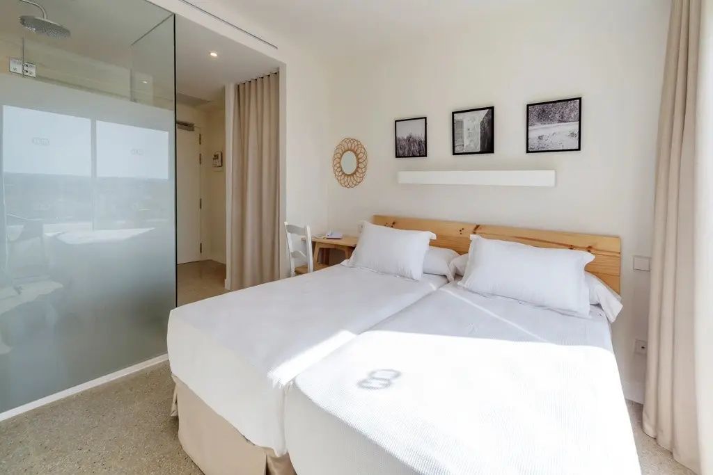 Helles Hotelzimmer mit zwei zusammengestellten Einzelbetten, Holzkopfteil und Wandbildern.