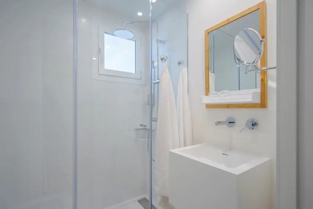 Badezimmer mit Dusche samt Regenduschkopf, weißem Waschbecken und Holzspiegel.