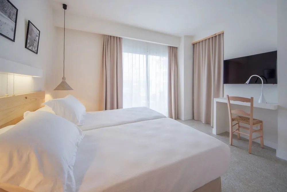 Hell gestaltetes Zimmer mit zwei Einzelbetten, Schreibtisch und beigen Vorhängen.