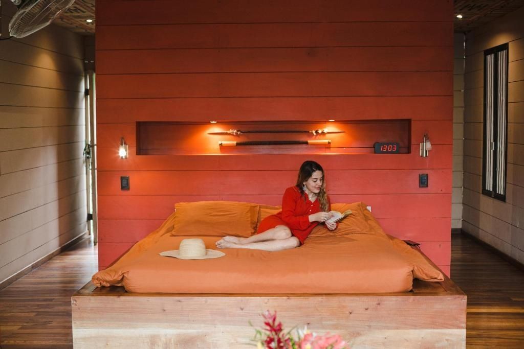 Doppelbett mit orangefarbener Bettwäsche vor einer roten Holzwand mit Beleuchtung.