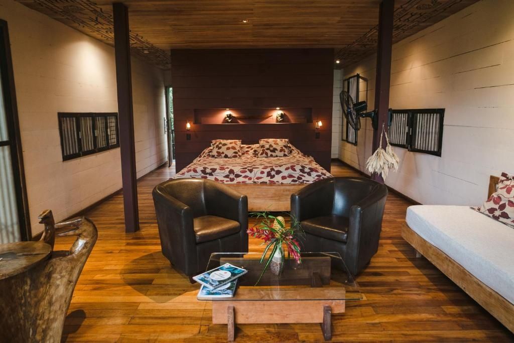 Schlafbereich mit Holzfußboden, zwei dunklen Ledersesseln und einem großen Doppelbett.