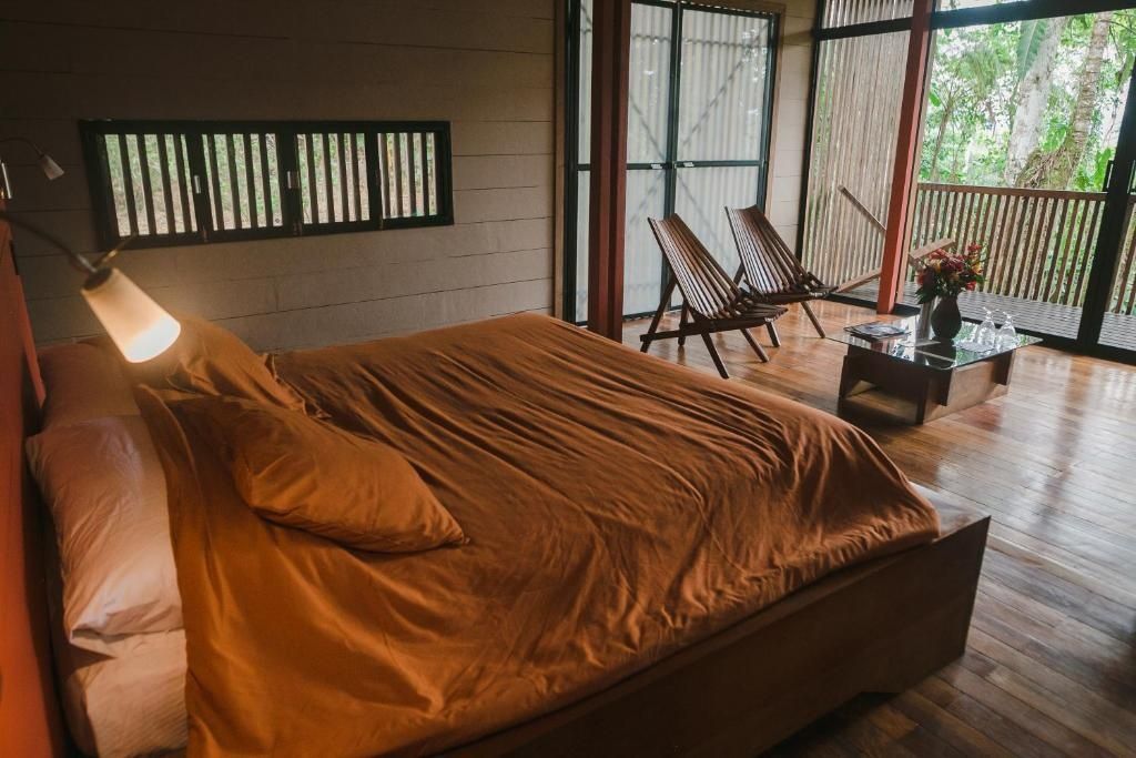 Großes Doppelbett mit orangefarbener Bettwäsche und Holzstühlen im Zimmer.