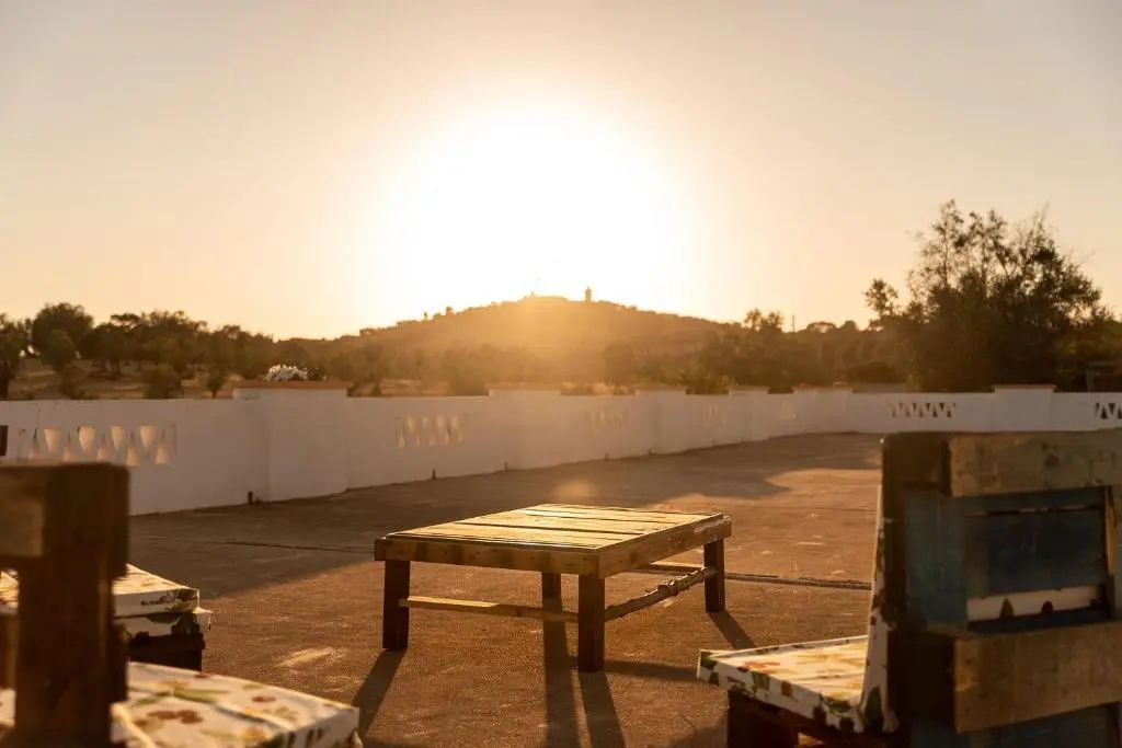 Sonnendurchflutete Terrasse mit Holztisch und Blick auf die Hügel bei Sonnenuntergang.