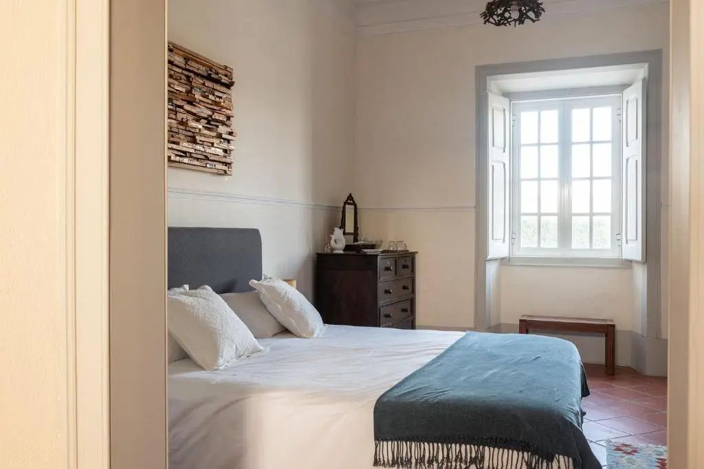 Hell eingerichtetes Schlafzimmer mit Doppelbett, Kommode aus Holz und einem Fenster.