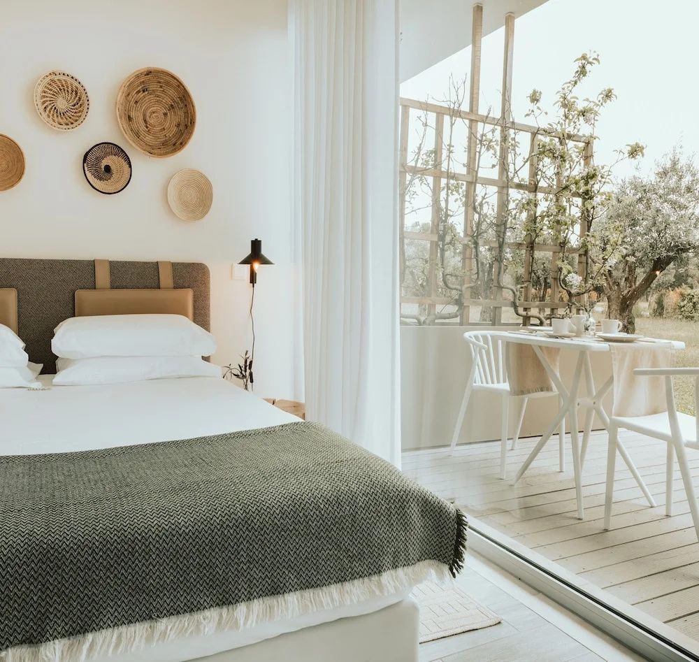 Helles Schlafzimmer mit Doppelbett, Wanddekoration aus Körben und Terrasse mit Sitzgelegenheit.