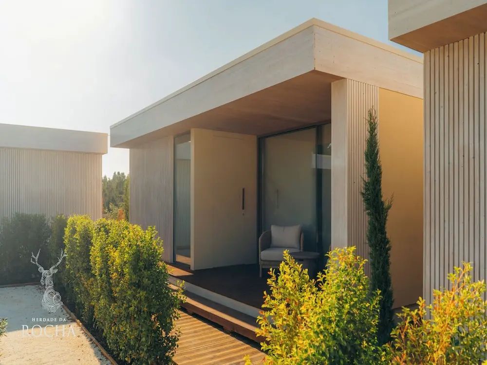 Moderne Lodge in Flachdachbauweise mit Holzterrasse, Sitzgelegenheit und Bepflanzung.